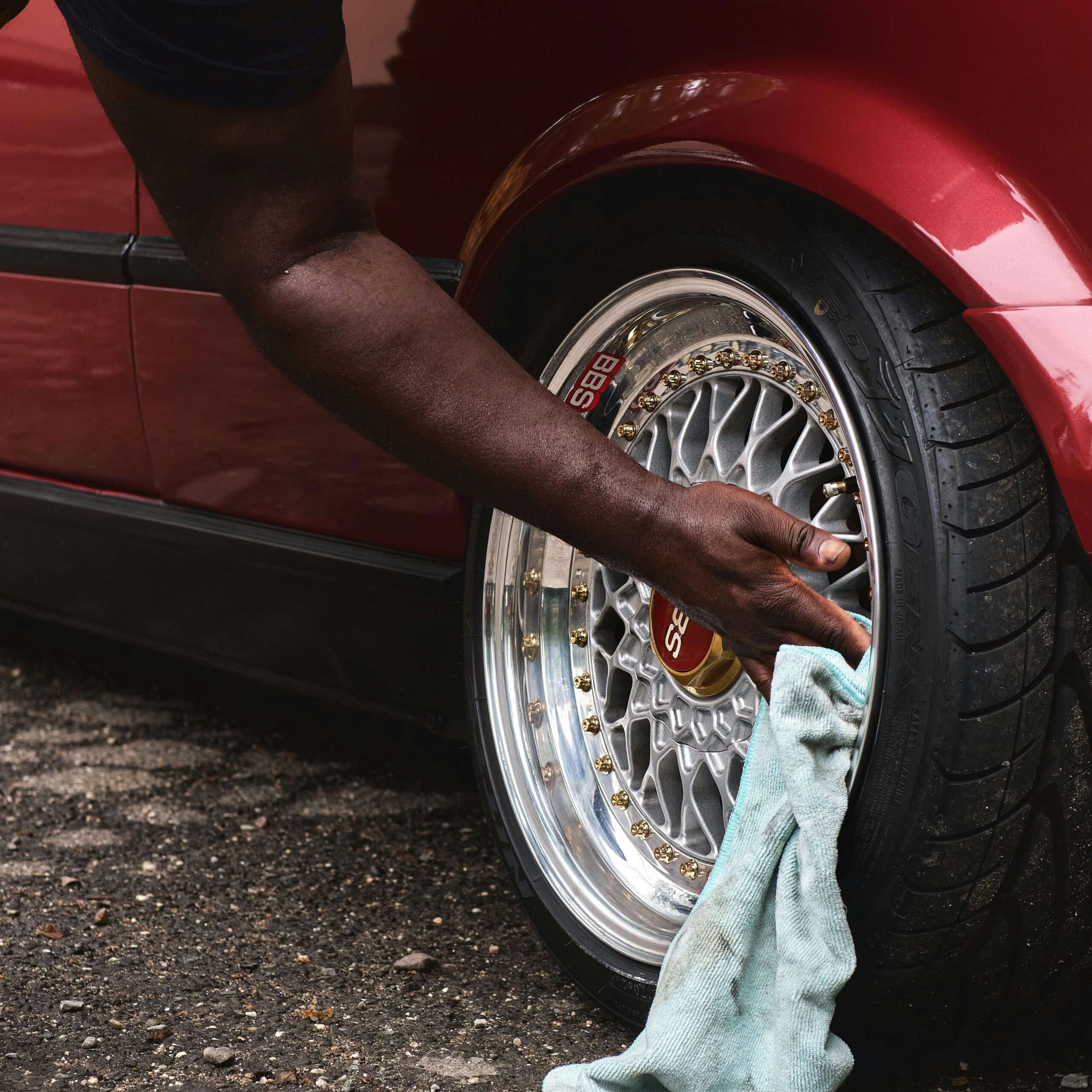 A man cleans a car wheel with a cloth, showcasing maintenance and care, outdoors on a street.